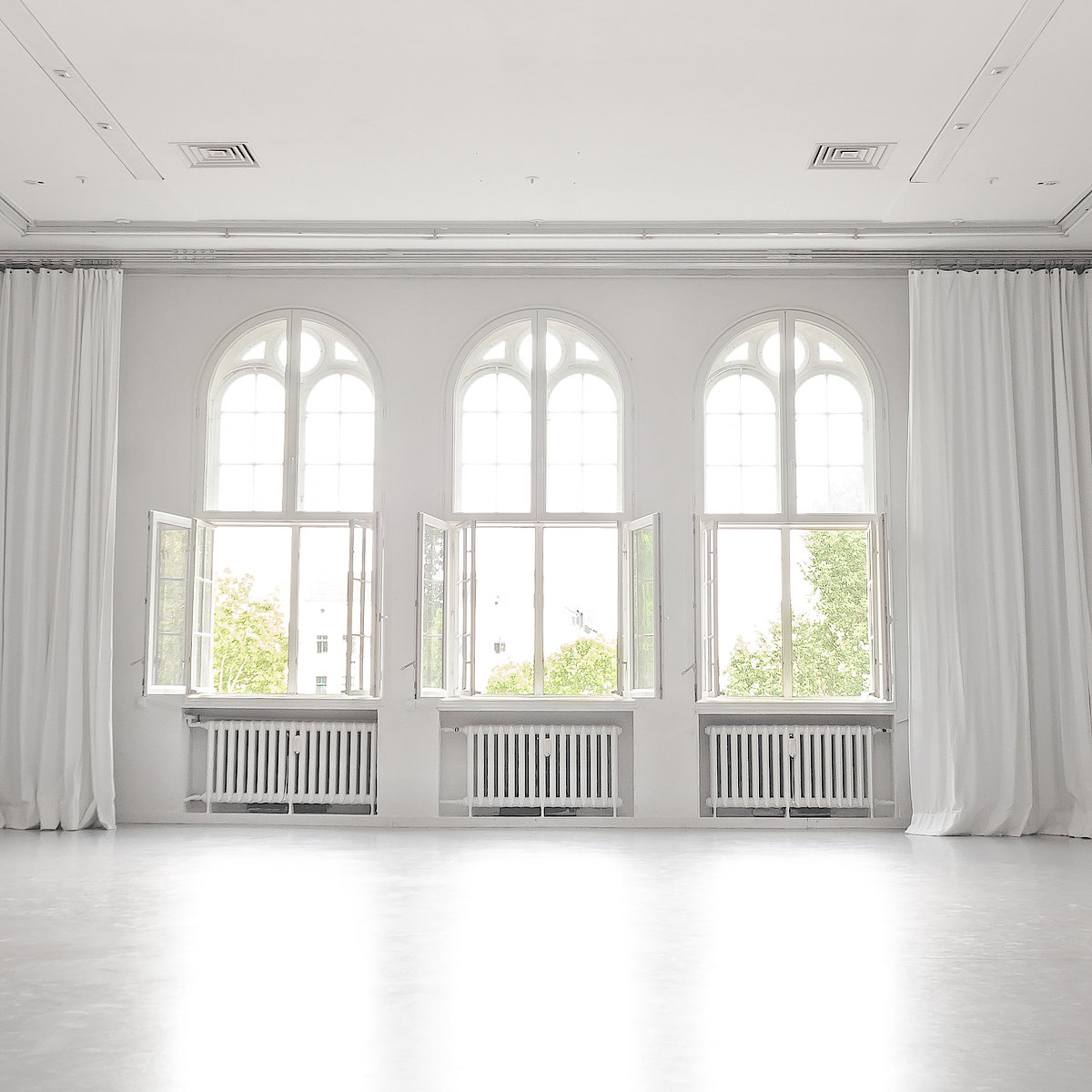 A picture of the studio.The walls, floor and curtains are white. The windows are open.