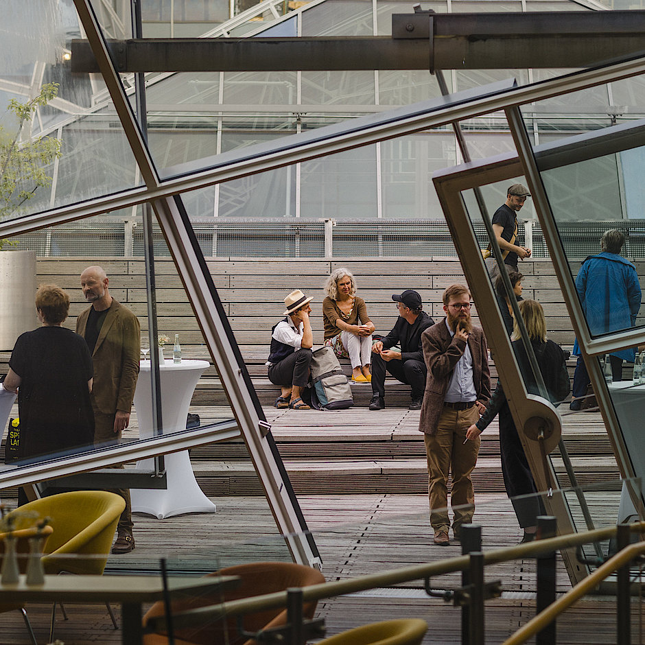 Ein Foto von der Preisverleihung in der Akademie der Künste. Sie können kleine Gruppen von Menschen sehen, die sich draußen auf der Terrasse unterhalten.