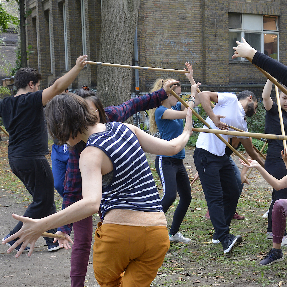 Participants of the Franco-German workshop do a theater exercise with a wooden stick they hold with the palm of their hand.