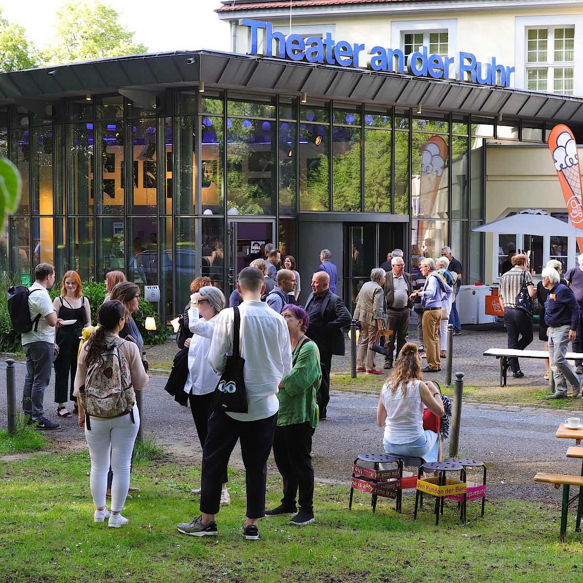 Photo from the closing ceremony of the festival "Stuecke" in front of the Theater an der Ruhr. You can see people talking in small groups with a glass in hand.