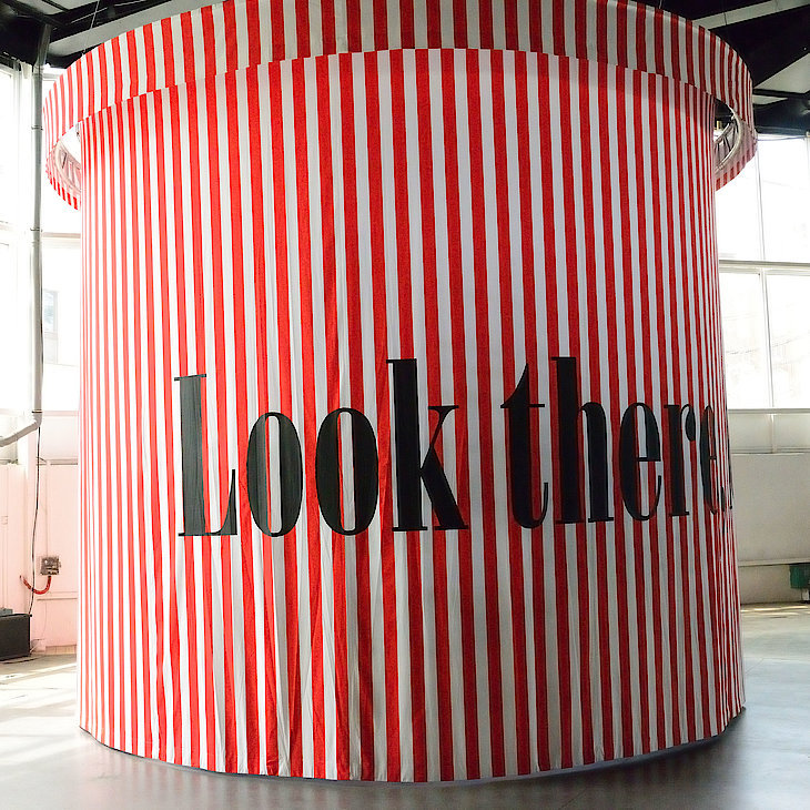 A work of art by the artist Bert Neumann. It is a large cylinder with red and white horizontal stripes. It reads "Look there".